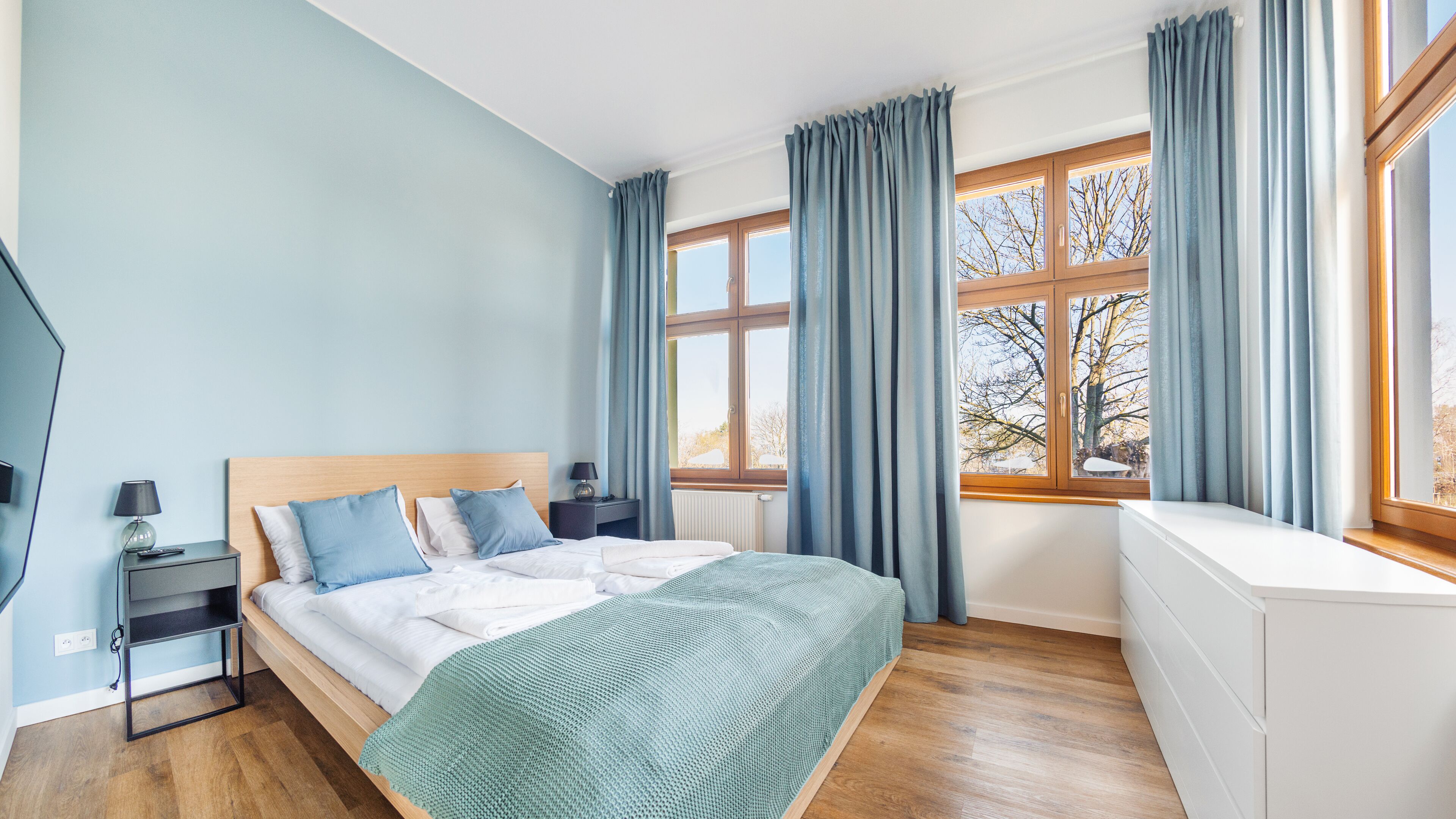 Een slaapkamer met een bed, nachtkastjes, een kaptafel en een raam met gordijnen.