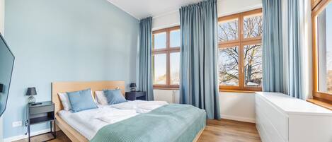 Een slaapkamer met een bed, nachtkastjes, een kaptafel en een raam met gordijnen.