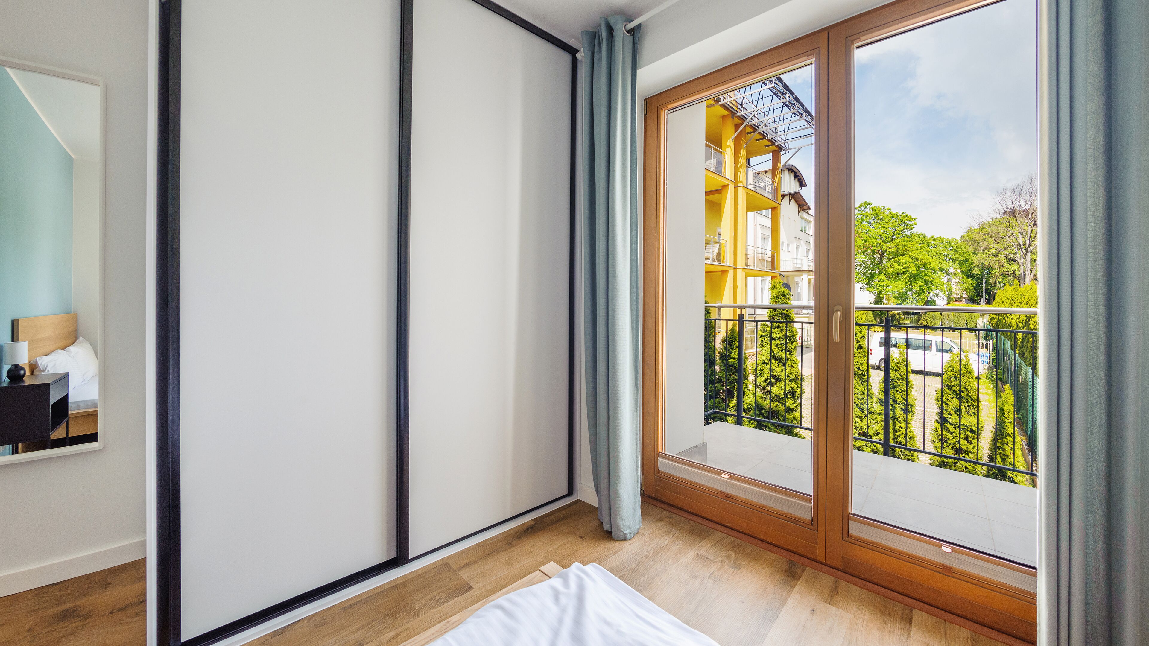 Ein Hotelzimmer mit einer großen Schiebeglastür, die auf einen Balkon mit Blick auf ein Gebäude und Bäume führt.