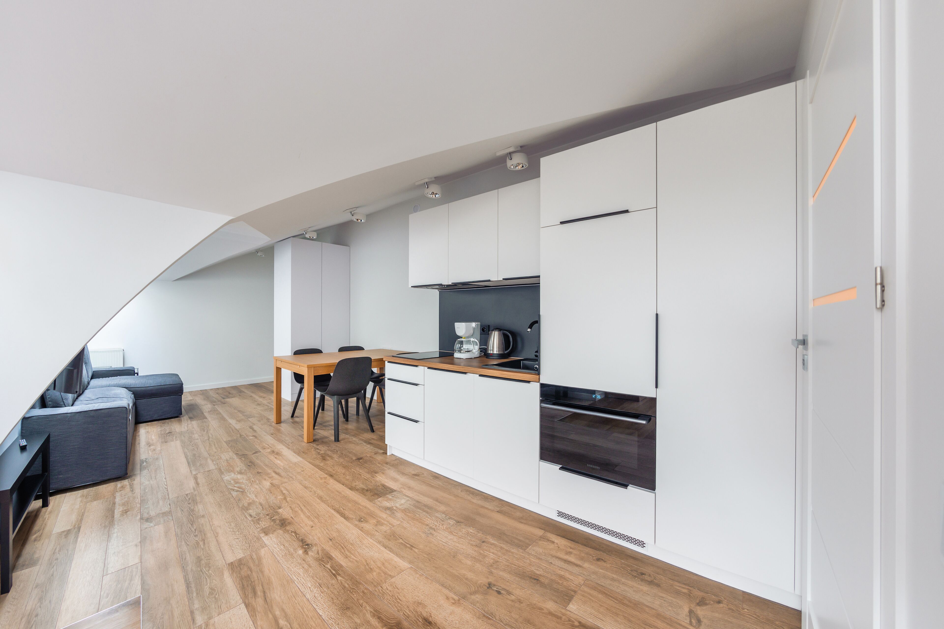 Una cocina moderna con armarios blancos, una mesa de comedor de madera y un horno empotrado.