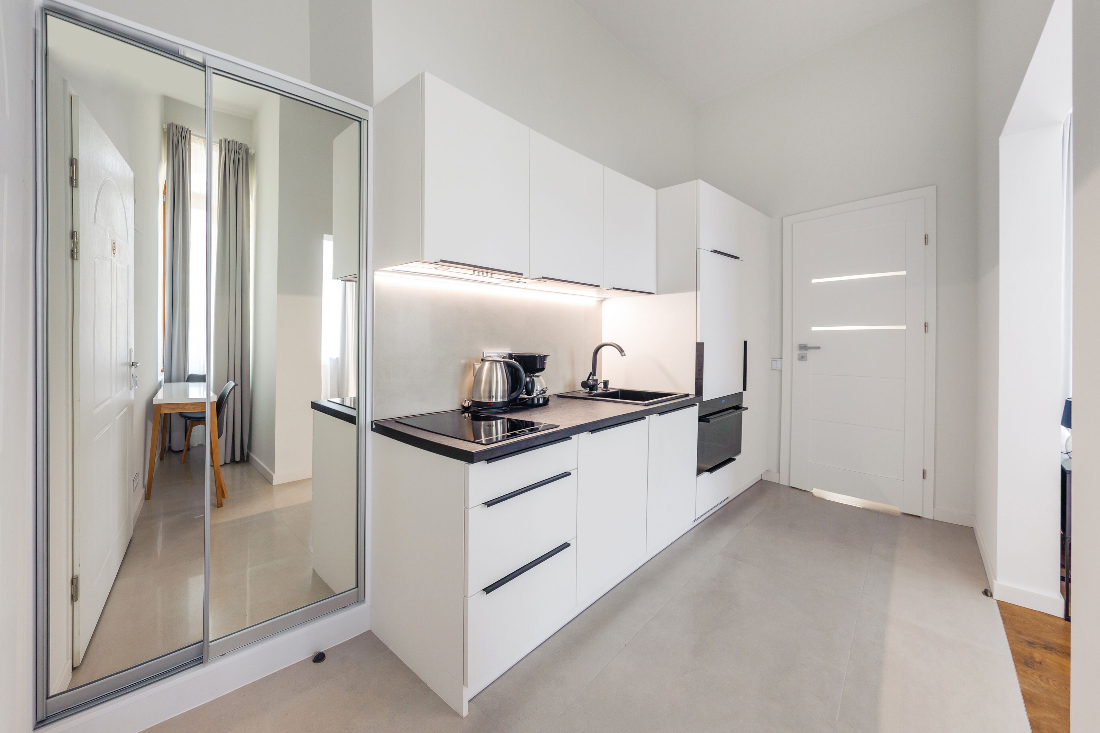 Une cuisine moderne avec des meubles blancs, un plan de travail noir et une bouilloire en acier inoxydable.