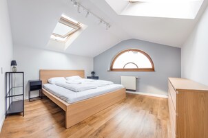 Un dormitorio con tragaluz, cama, mesita de noche, lámpara y radiador.