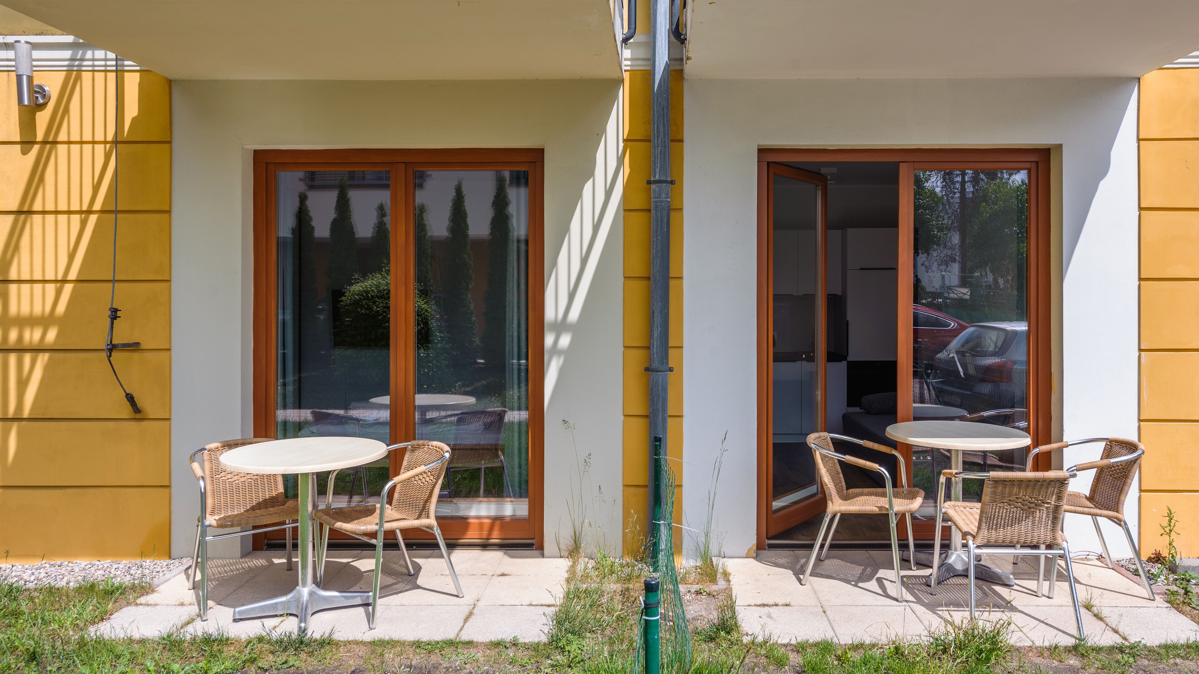 A patio with two round tables and wicker chairs, a yellow wall, and a glass door leading to an outdoor area.