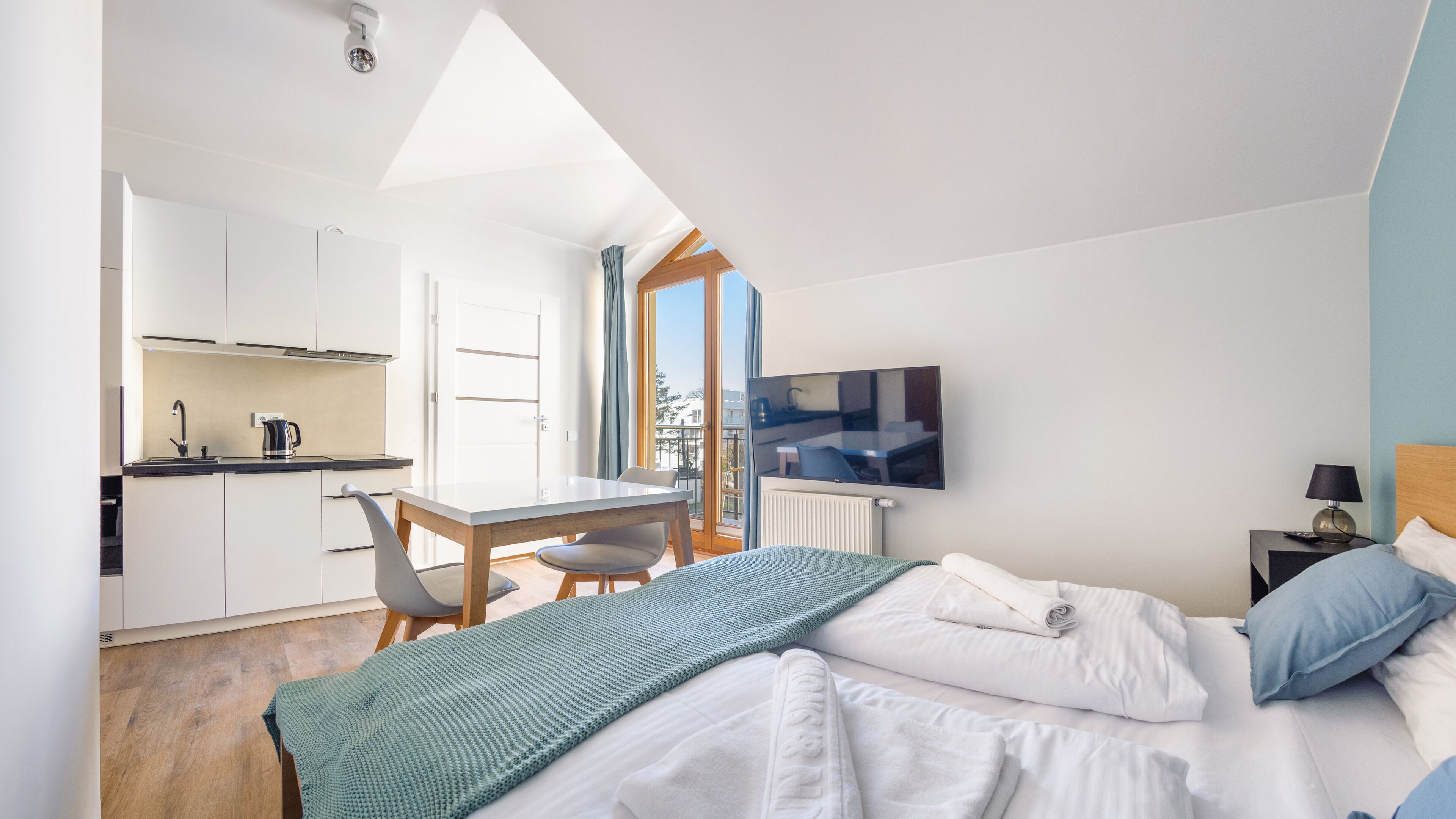 Ein modernes Hotelzimmer mit Küchenzeile, einem Esstisch und einem Bett mit Fernseher.