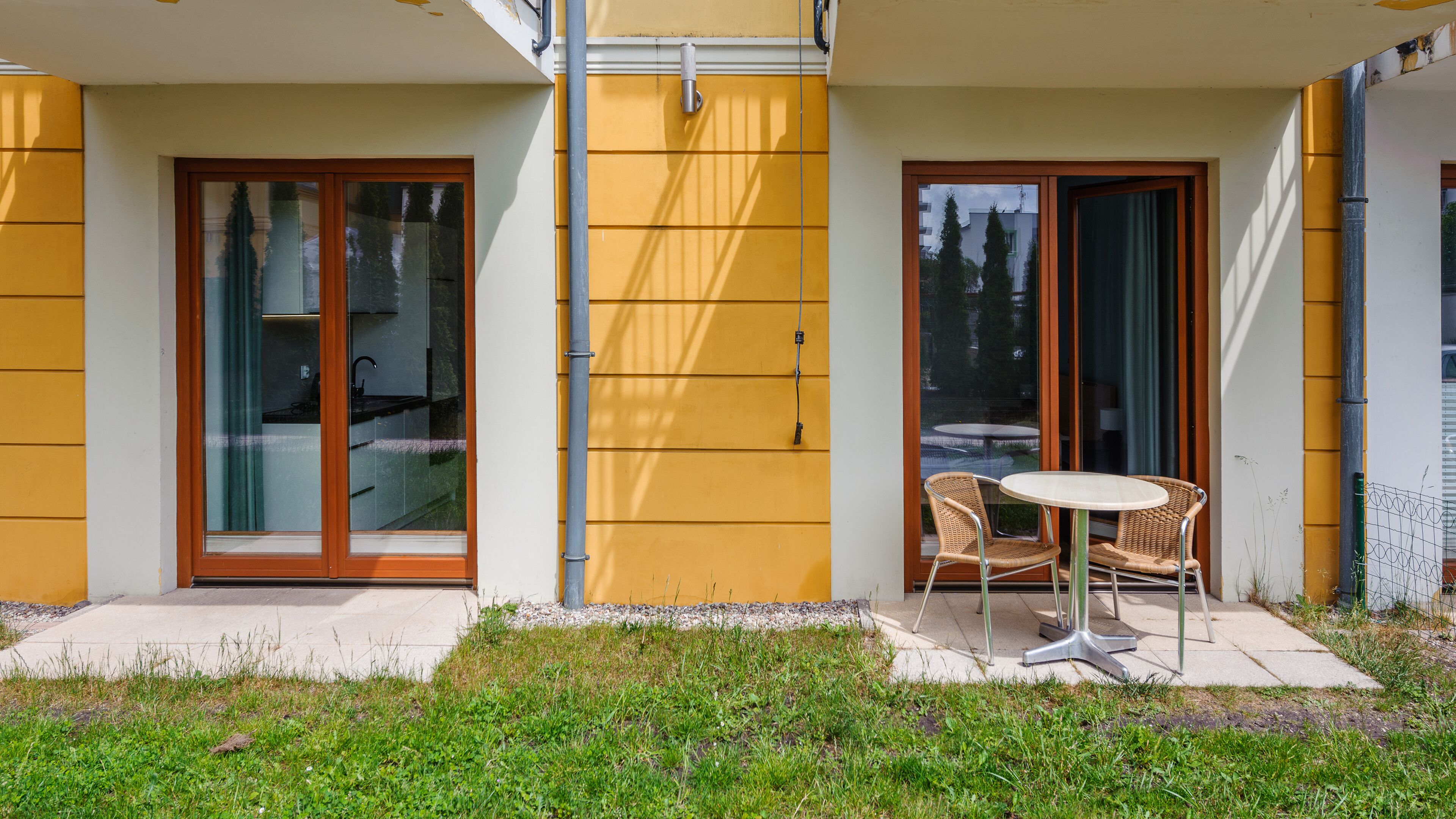 Un edificio moderno con pareti esterne gialle, ampie porte scorrevoli in vetro e una piccola area esterna con tavolo e sedie.