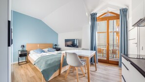 A modern hotel room with a bed, a desk, a chair, a TV, and a balcony with curtains.