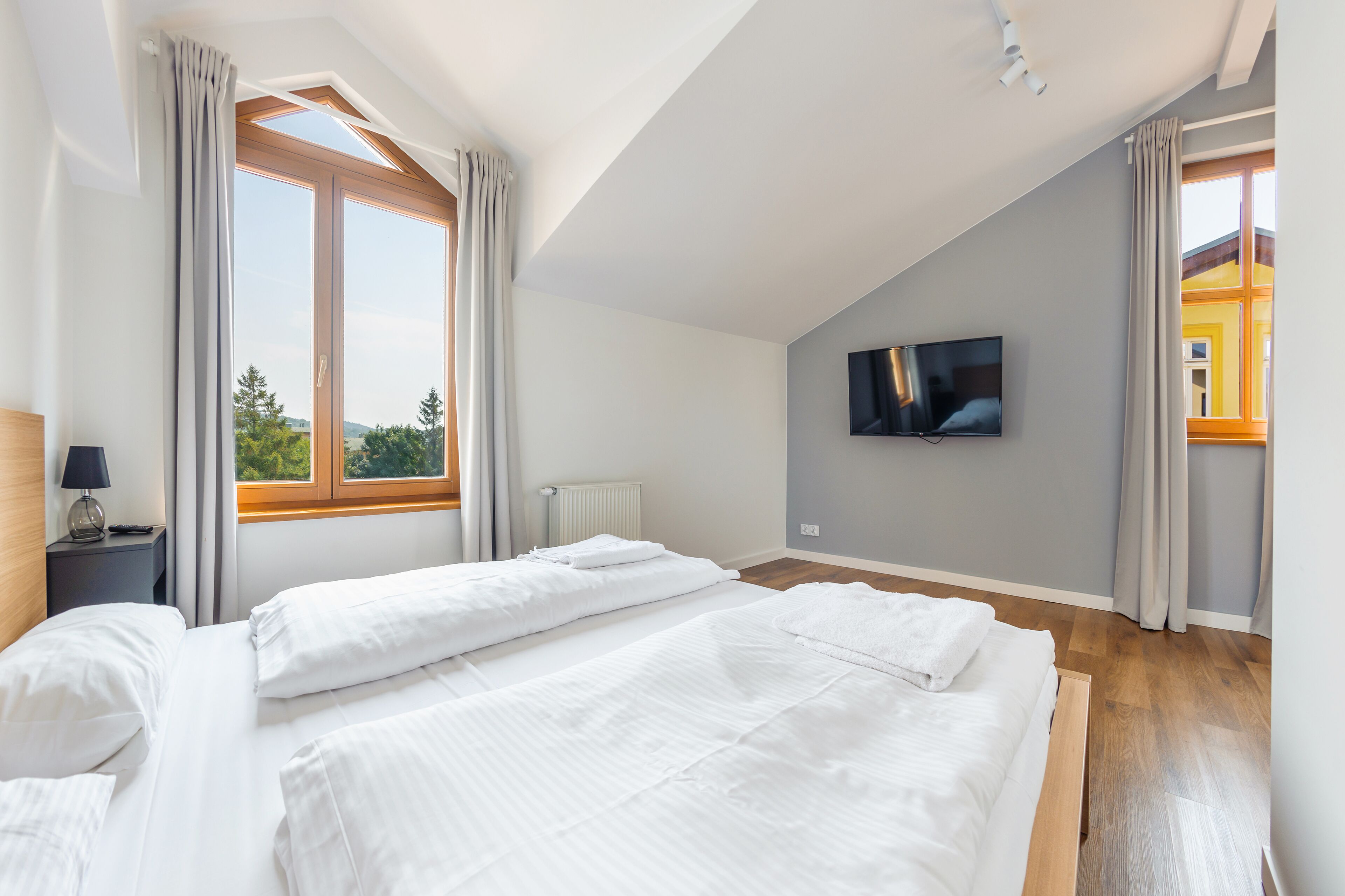 A bedroom with two beds, a TV on the wall, and large windows with curtains.