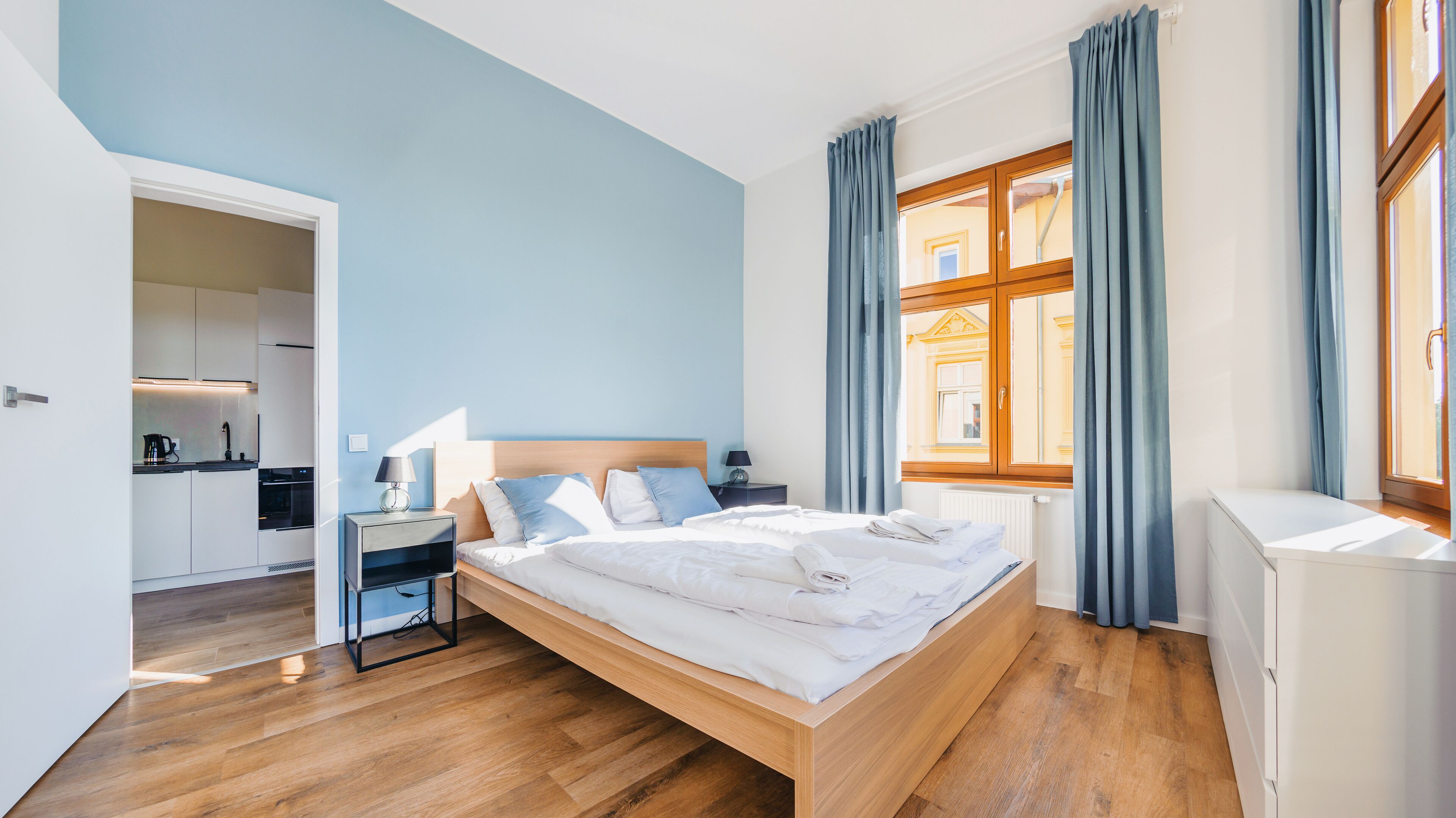 Une chambre moderne avec un lit en bois, des tables de chevet, une commode et une fenêtre avec des rideaux.