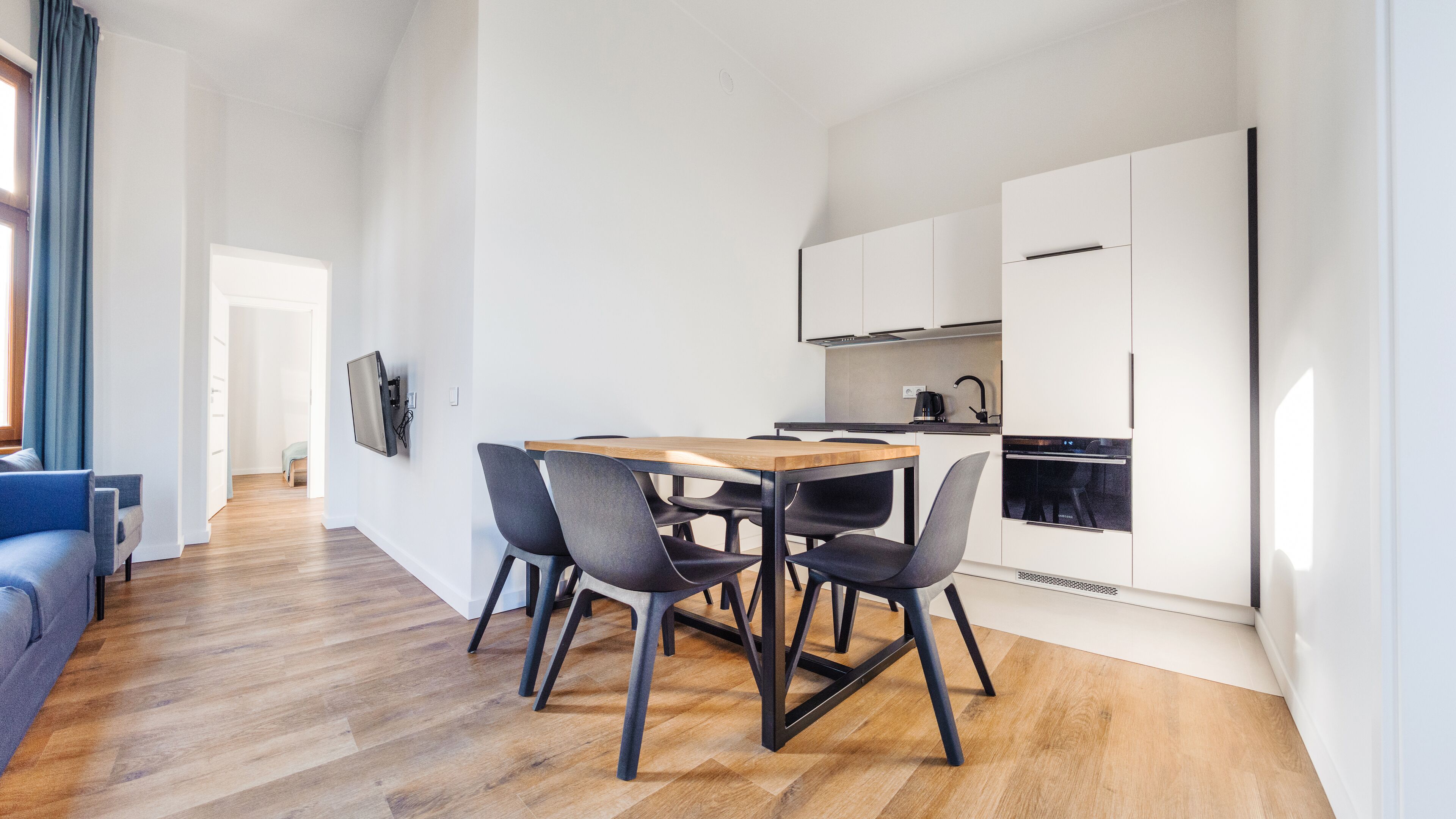 Une cuisine moderne avec des meubles blancs, une table à manger en bois et des chaises noires.