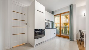 A modern kitchen with white cabinets, a built-in oven, and a window with a view of a balcony.