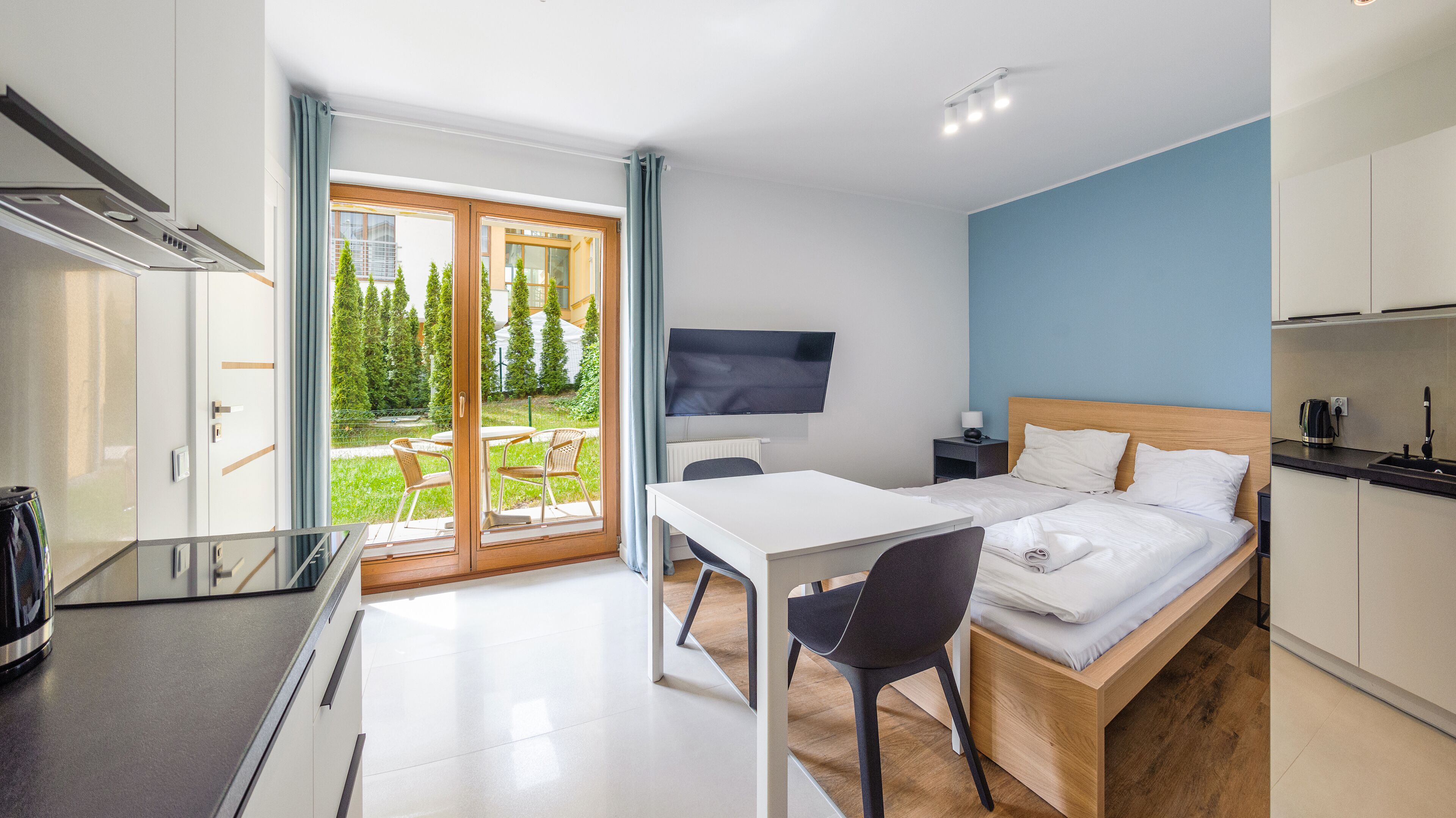 Habitación de hotel moderna con cama, escritorio, silla, televisor y vistas a un jardín verde.