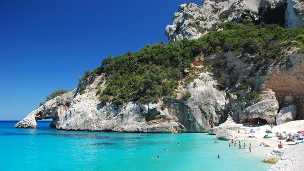 A coastal beach with clear turquoise water, rocky cliffs, and a sandy area with umbrellas. - B&BIssicoro Baunei (Baunei)
