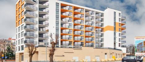 A multi-story residential building with balconies, a brick facade, and a clear sky.
