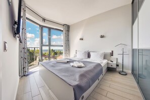 Ein modernes Schlafzimmer mit einem großen Bett, einem Nachttisch, einer Stehlampe und einem Balkon mit Blick.