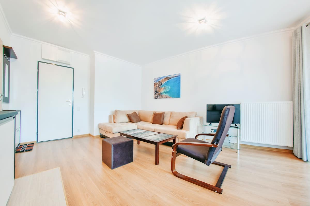 Una sala de estar moderna con sofá, mesa de centro y sillón reclinable. Hay un televisor de pantalla plana y un cuadro en la pared.