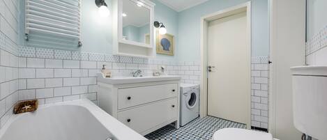 A bathroom with a bathtub, a sink, a mirror, a toilet, and a washing machine.