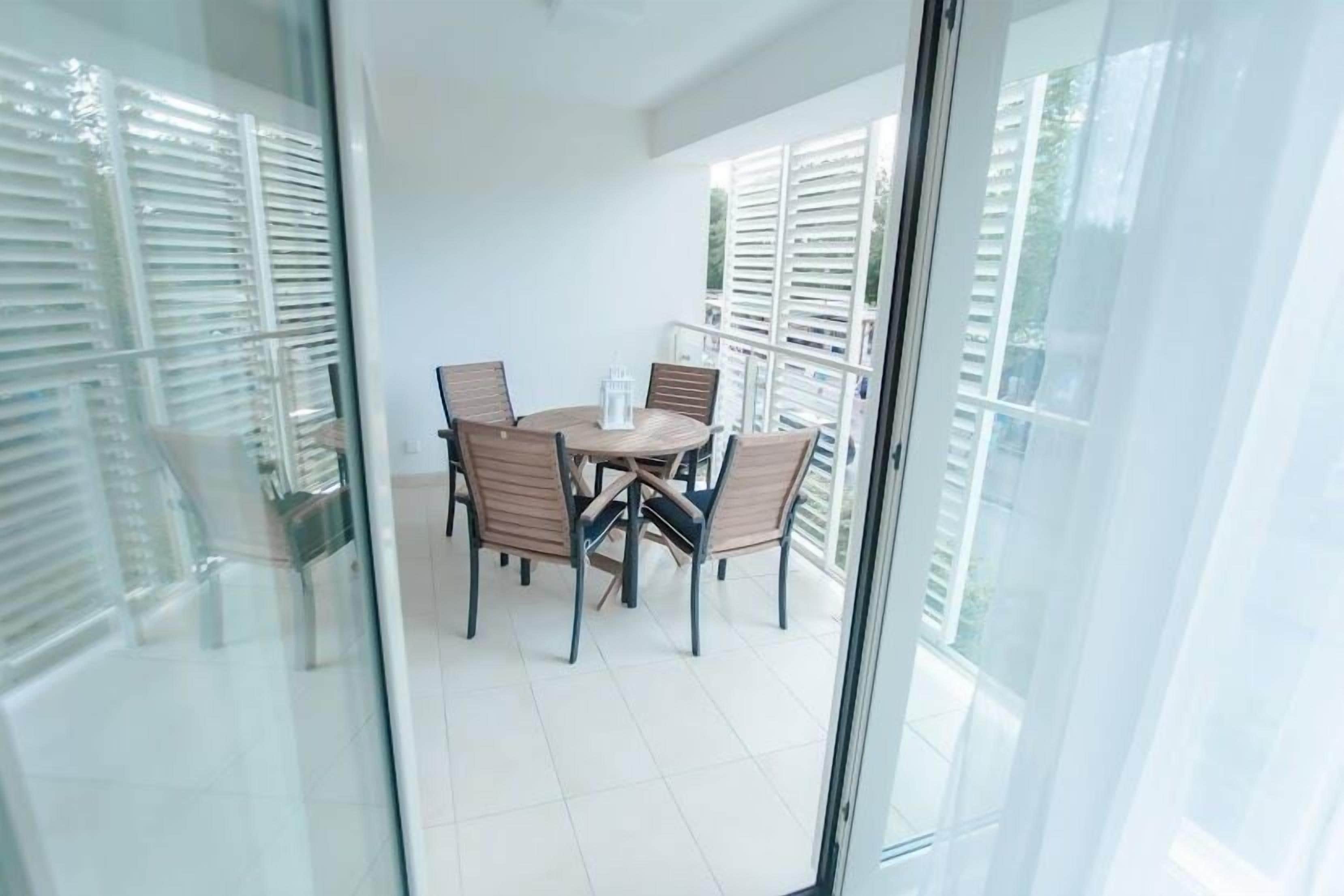 A balcony with a table and chairs, large windows with blinds, and a view of the outside.