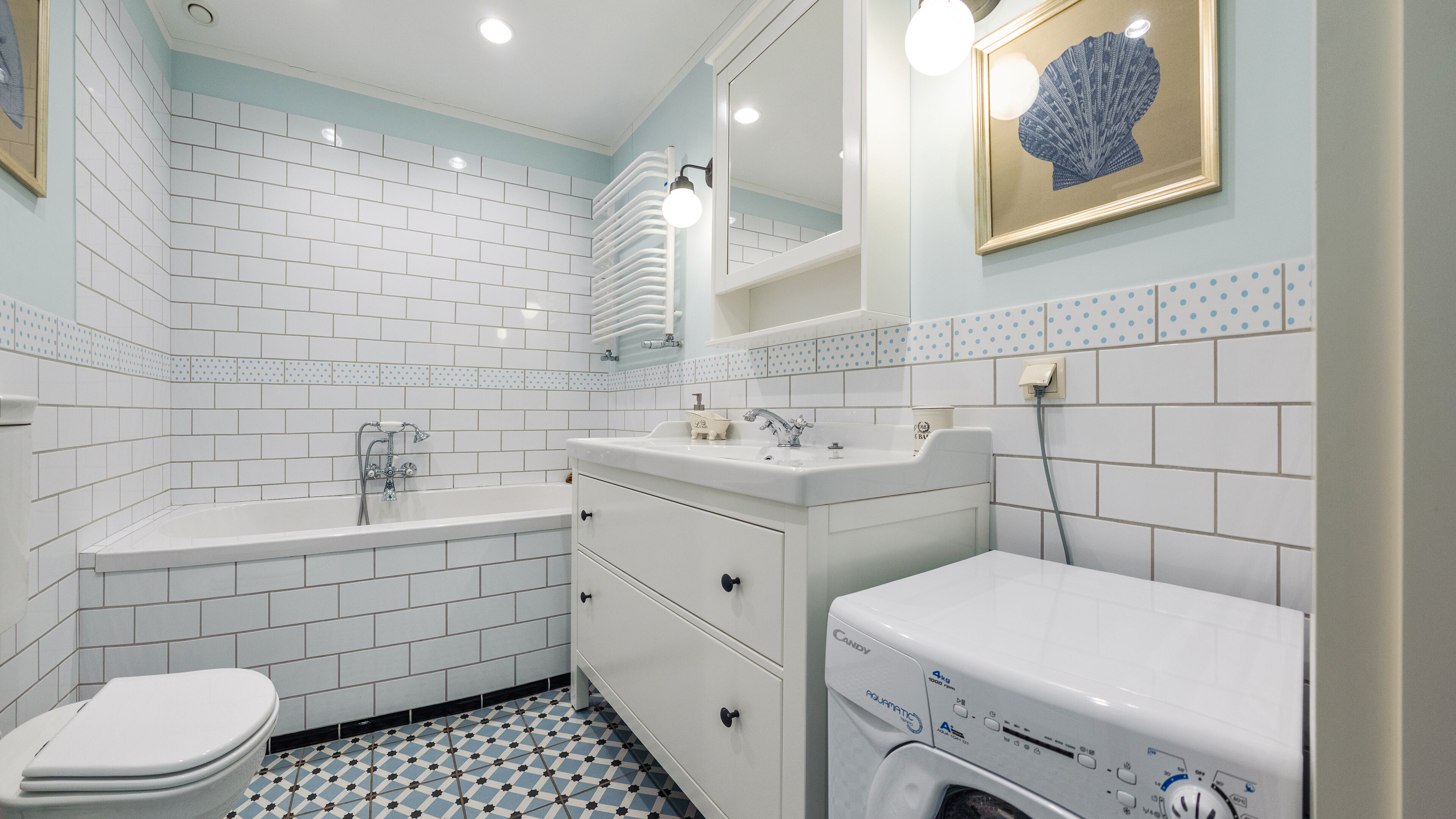 A bathroom with white subway tiles, a bathtub, a sink, a toilet, and a washing machine.
