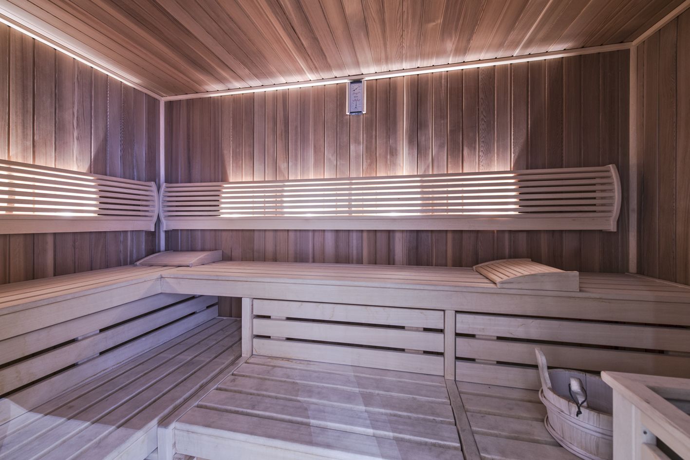 Een sauna met houten banken en lambrisering, met een bank voorzien van een ingebouwd zitgedeelte en een kleine emmer.