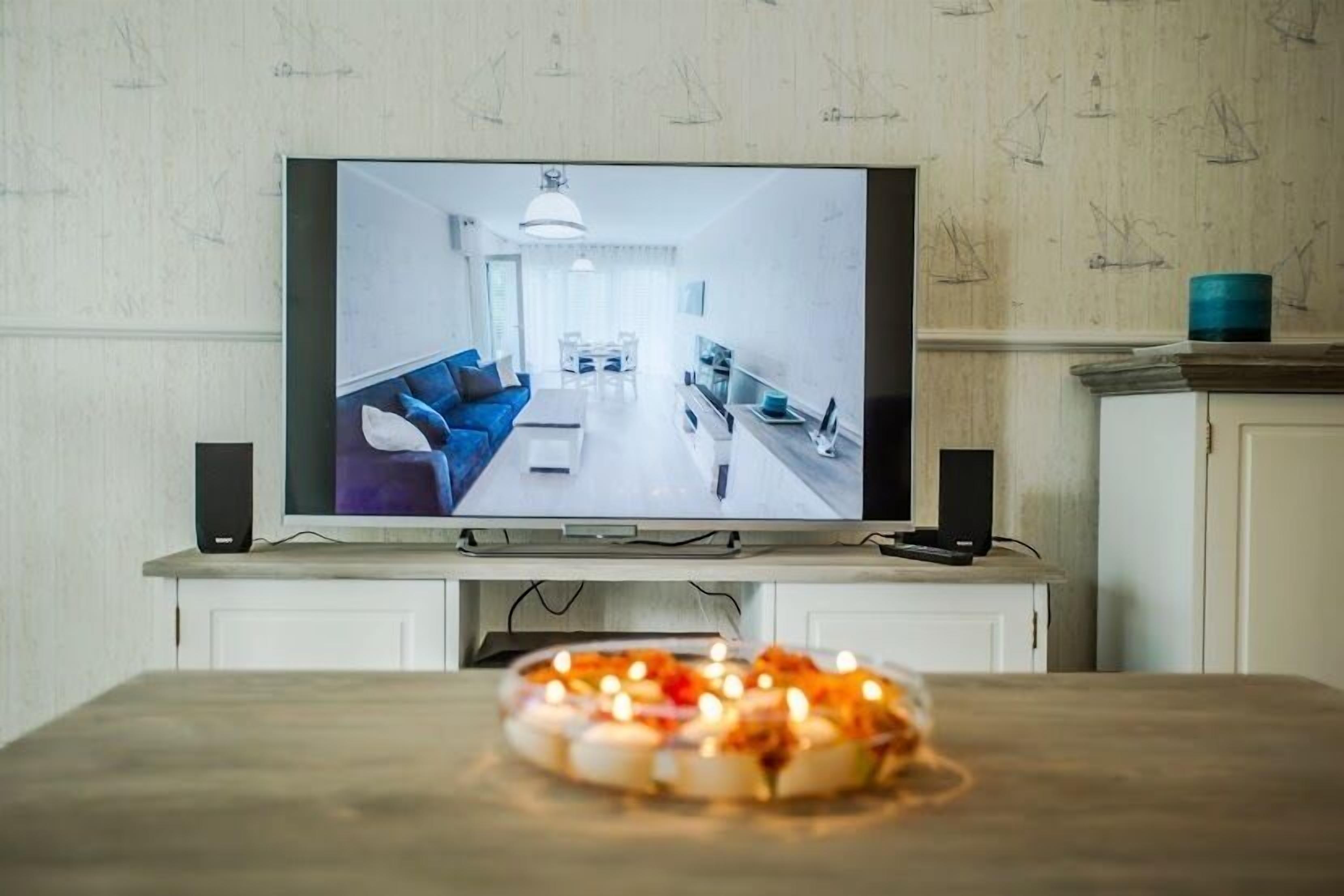 Un téléviseur diffusant une image d’un salon moderne, avec un canapé, une table basse et un coin repas.