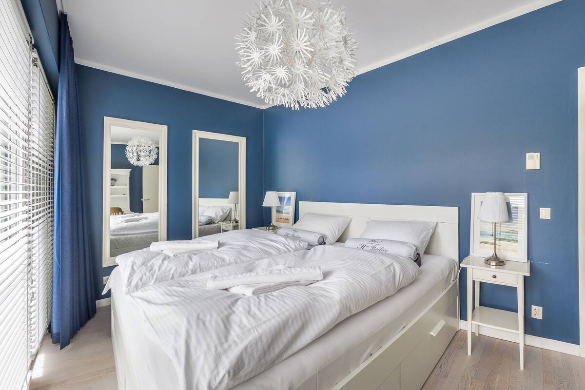 A bedroom with a large bed, two bedside tables, a mirror, and a unique chandelier.