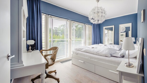 A bedroom with a bed, a desk, a chair, and a large window with blinds. - Apartamenty Sun & Snow Playa Baltis (Miedzyzdroje)