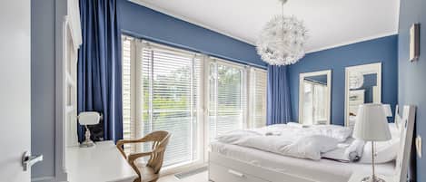 A bedroom with a bed, a desk, a chair, and a large window with blinds.
