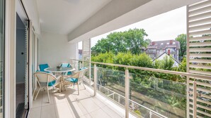 A balcony with a glass railing, wicker furniture, and a view of a residential area. - Apartamenty Sun & Snow Playa Baltis (Miedzyzdroje)