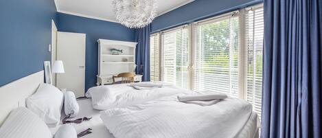 A bedroom with a bed, a desk, a chair, a wardrobe, and a window with blinds.