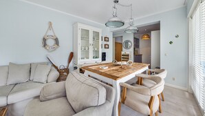 A modern living room with a wooden dining table, beige sofa, and white cabinetry. - Apartamenty Sun & Snow Playa Baltis (Miedzyzdroje)