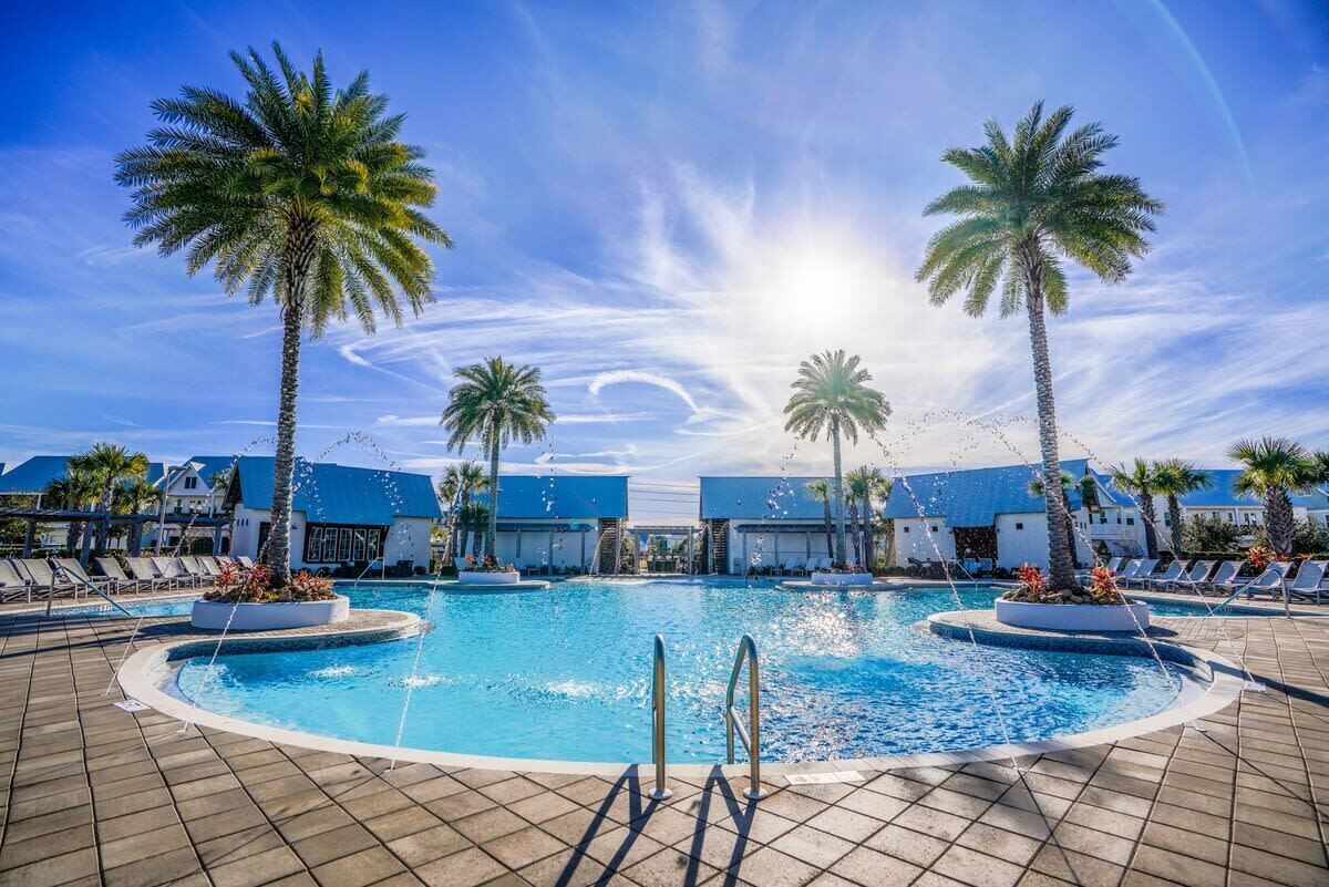 Piscina con palmeras, sillas de descanso y cielo despejado.