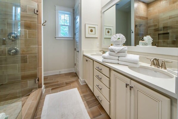 Un baño con cabina de ducha de vidrio, un lavabo blanco con grifo dorado y un espejo grande sobre el mueble.