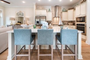 Cozinha moderna com armários brancos, uma ilha central com banquetas, eletrodomésticos de aço inoxidável e detalhes decorativos.