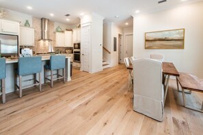 A modern kitchen with wooden flooring, white cabinetry, and a dining area with a table and chairs. - 3BR Townhome w/ 6-Seater Golf Cart & Bikes ~ Serenity Shores at Prominence North (Inlet Beach)