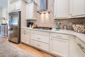 A modern kitchen with white cabinetry, a stainless steel refrigerator, a gas stove, and a stone backsplash.