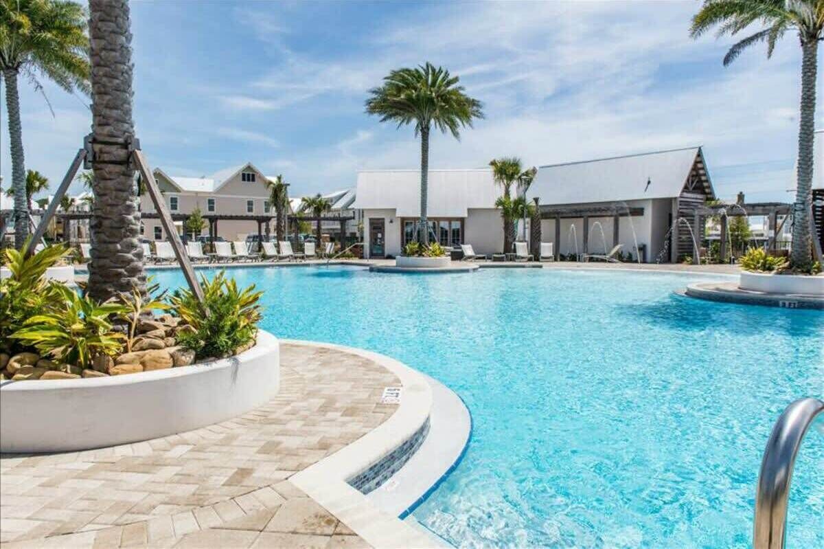 A swimming pool with lounge chairs and palm trees, surrounded by buildings with a modern design.