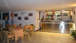 A bar area with a stainless steel counter, wicker chairs, and a small table with a red object on it.