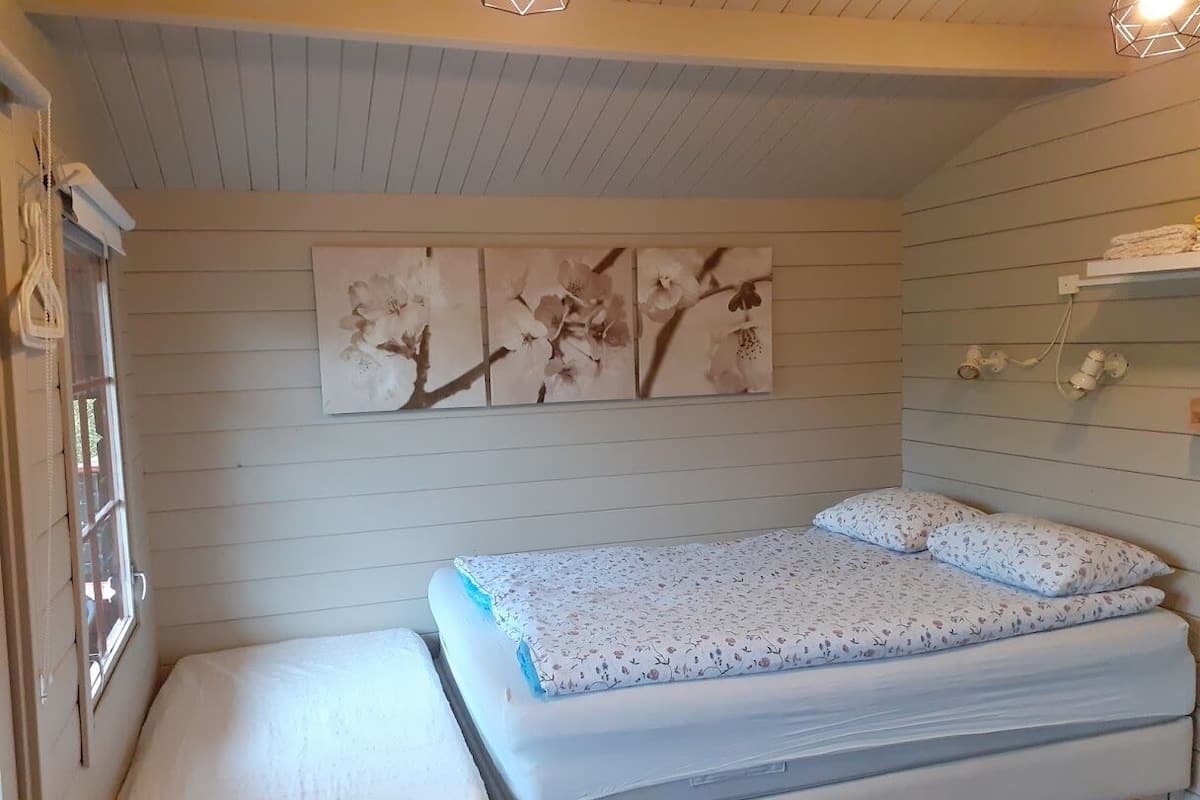 A small, cozy bedroom with a single bed, a window with blinds, and a wall-mounted shelf with towels.
