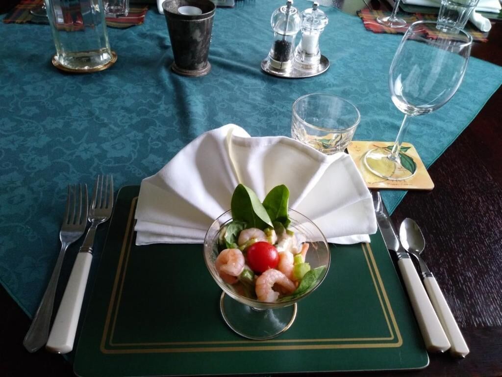 Una mesa de comedor bien dispuesta con un mantel individual verde, un bol de vidrio transparente con ensalada de camarones y una servilleta blanca doblada sobre el mantel.