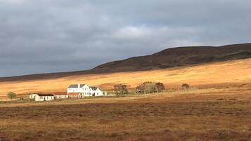 A rural landscape with a white building, possibly a farmhouse, surrounded by open fields and a hill in the background.