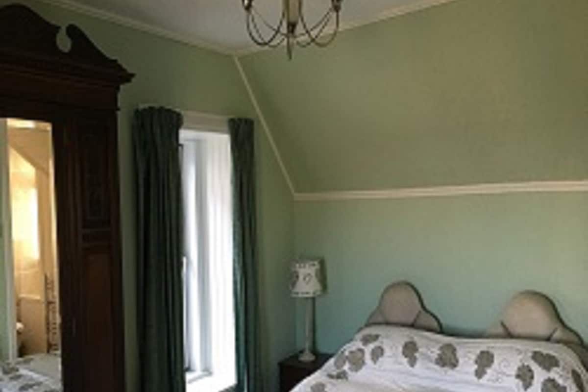 Une chambre à coucher avec un lit, une table de chevet, un miroir et une fenêtre avec des rideaux.