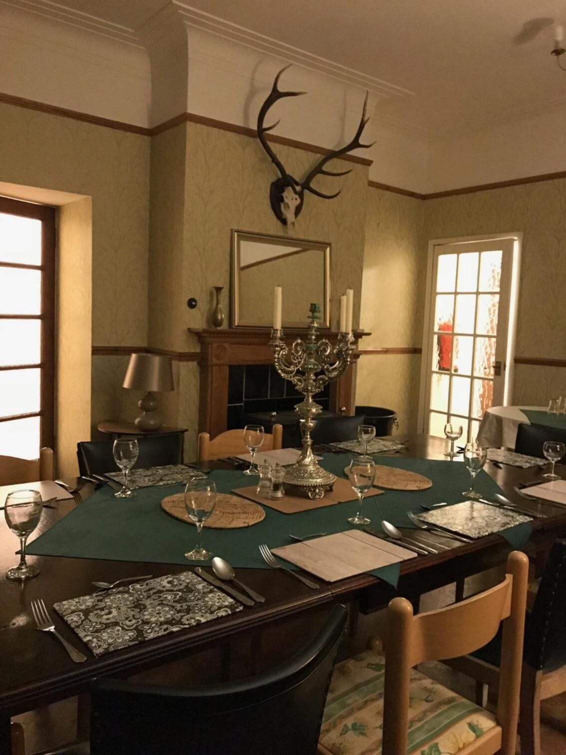 A dining room with a large table set for six, a chandelier, and a mounted deer head on the wall.