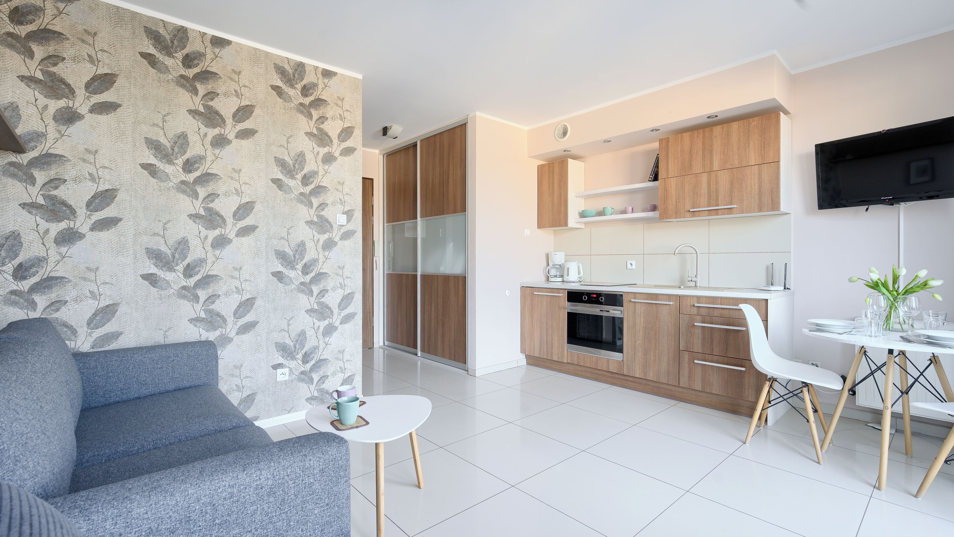 Una cocina moderna con armarios de madera, horno empotrado y comedor con mesa y sillas blancas.