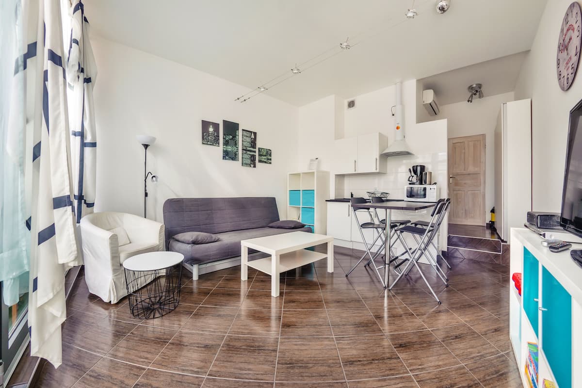 A modern living room with a sofa, coffee table, and dining area. There is a kitchen in the background with a refrigerator and a microwave.