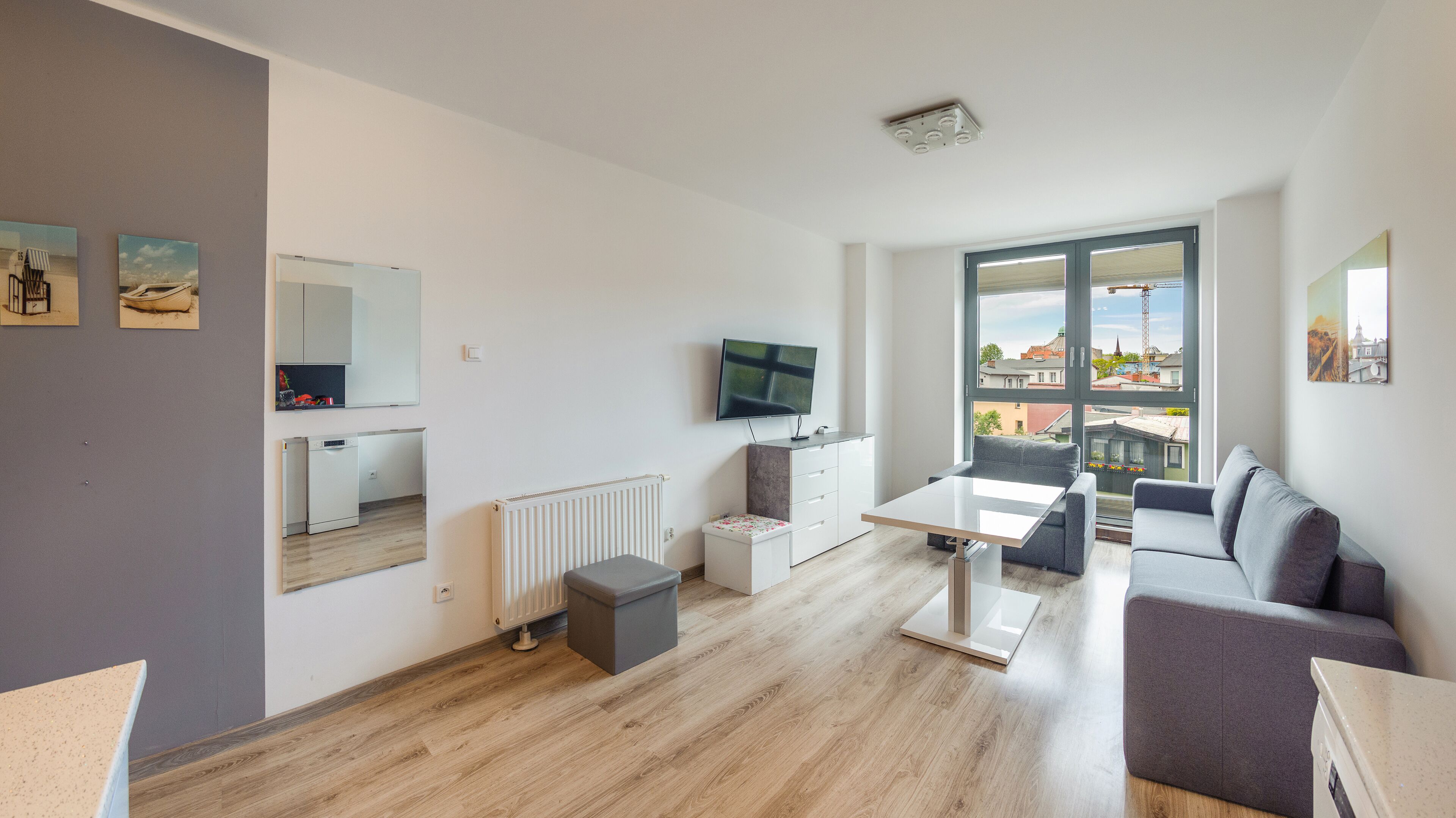 A modern living room with a sofa, a coffee table, a TV, and a view of the city through large windows.
