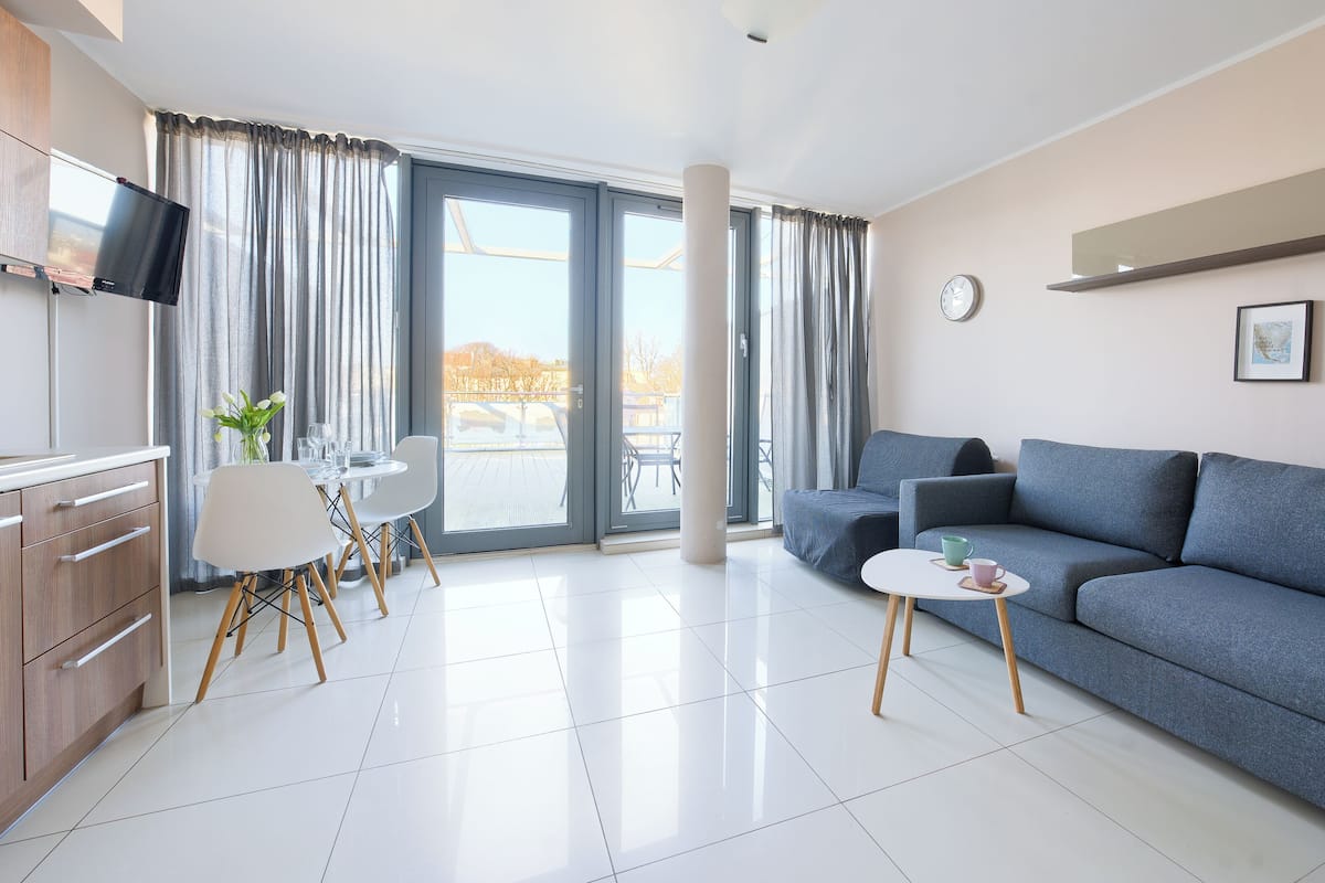 A modern living room with a grey sofa, a small white table, and a dining area with a white table and chairs.