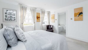 Une chambre avec un grand lit, une chaise et des œuvres d’art accrochées aux murs.