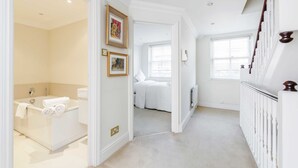 Une salle de bain moderne avec une baignoire, des toilettes et une douche. Les murs sont ornés de tableaux encadrés et il y a une fenêtre avec des stores.