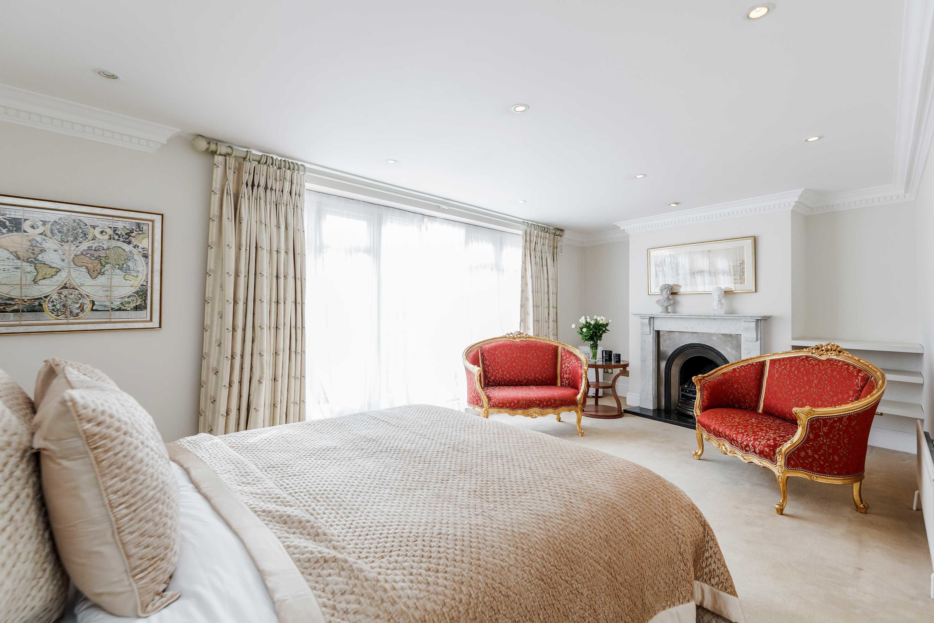 A spacious bedroom with a large bed, two red armchairs, a fireplace, and a world map on the wall.