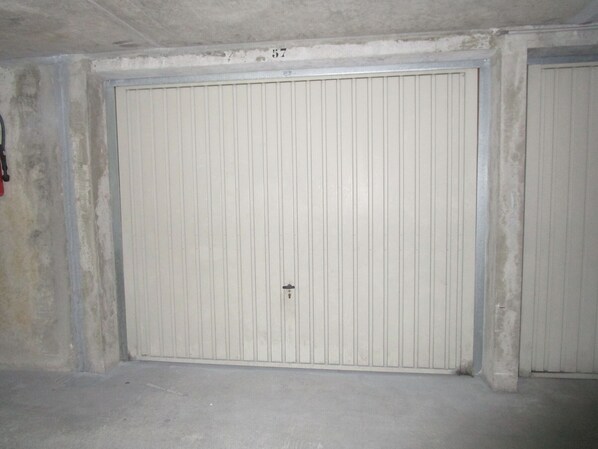 Une grande porte blanche, sans ornement, avec un trou de serrure au centre, située dans une pièce aux murs et au sol en béton.